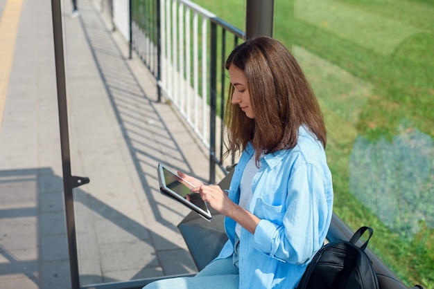 Happy woman uses a tablet or ebook on a tram station while waiting for public transport.