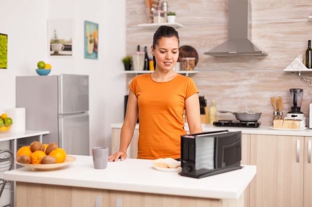 Happy woman using electric toaster in the morning wife roasting bread slices on electric toaster