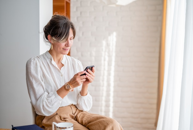 Happy woman using mobile phone while working at homeBeautiful lady browsing website on phone