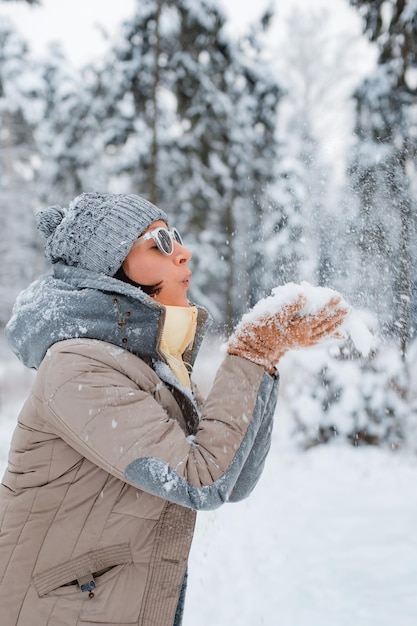 Happy woman walking outdoors on a snowy winter day Female model dressed in grey blowing snow having fun