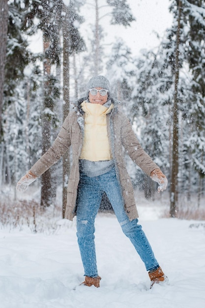 Happy woman walking outdoors on a snowy winter day Female model dressed in grey blowing snow having fun