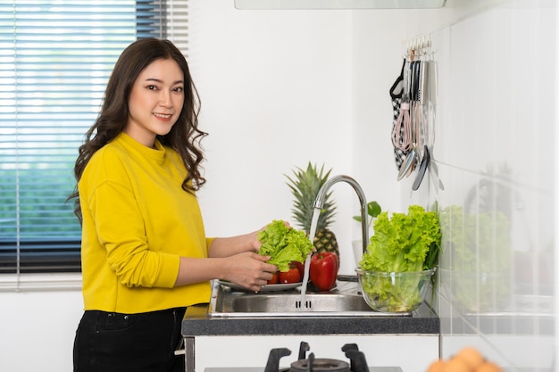 Happy woman washing vegetables in the sink in the kitchen at home