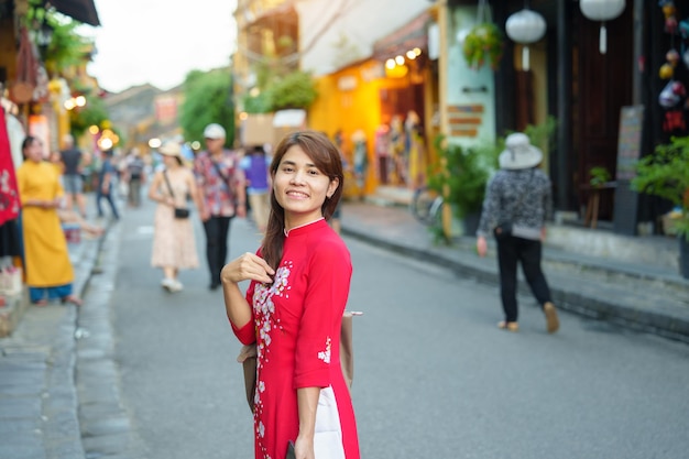 Happy woman wearing Ao Dai Vietnamese dress asian traveler sightseeing at Hoi An ancient town in central Vietnam landmark and popular for tourist attractions Vietnam and Southeast travel concept