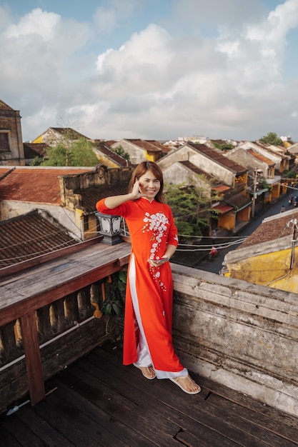 Happy woman wearing Ao Dai Vietnamese dress traveler sightseeing view at rooftop at Hoi An ancient town in Vietnam landmark and popular for tourist attractions Vietnam and Southeast travel concept