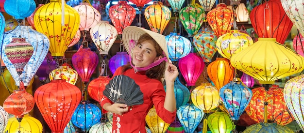 Happy woman wearing Ao Dai Vietnamese dress with colorful lanterns traveler sightseeing at Hoi An ancient town in central Vietnamlandmark for tourist attractionsVietnam and Southeast travel concept