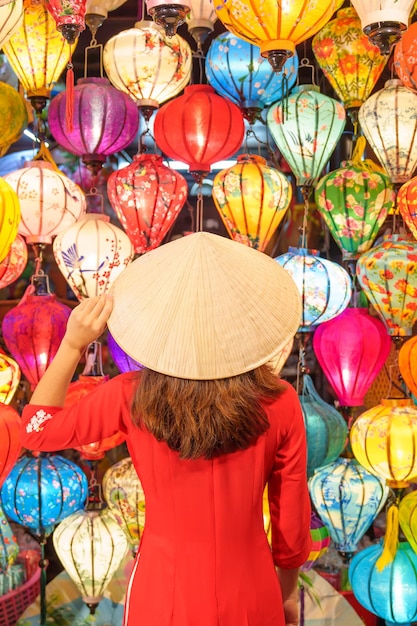 Happy woman wearing Ao Dai Vietnamese dress with colorful lanterns traveler sightseeing at Hoi An ancient town in central Vietnamlandmark for tourist attractionsVietnam and Southeast travel concept