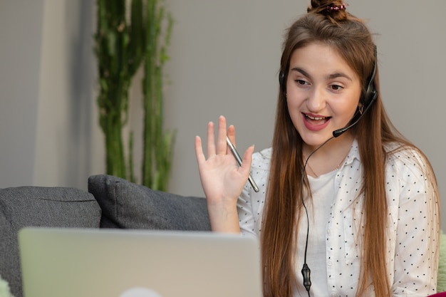 Photo happy woman wearing headphones greeting during a video conference on line with a red laptop sitting in a table in the living room.