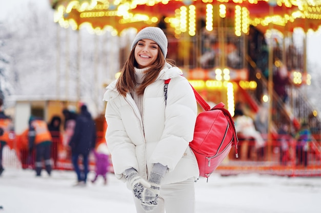 Happy woman in white coat walks at the christmas fair while holds backpack lifestyle holidays