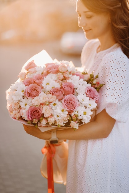 A happy woman in a white dress at sunset with a bouquet of flowers in the city