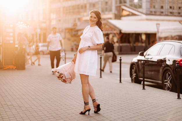 A happy woman in a white dress at sunset with a bouquet of flowers in the city