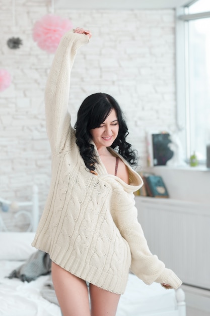 Happy woman in white sweater stretching arms in bedroom