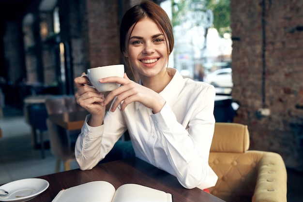 Happy woman with a cup in hand sits in a chair in the restaurant and interior in the background High quality photo