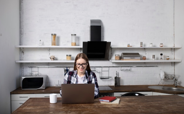 Happy woman with glasses working at home in the morning. Girl drinking coffee. She is using her laptop