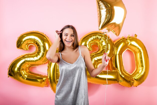 Happy woman with golden new year 2020 balloons isolated over pink