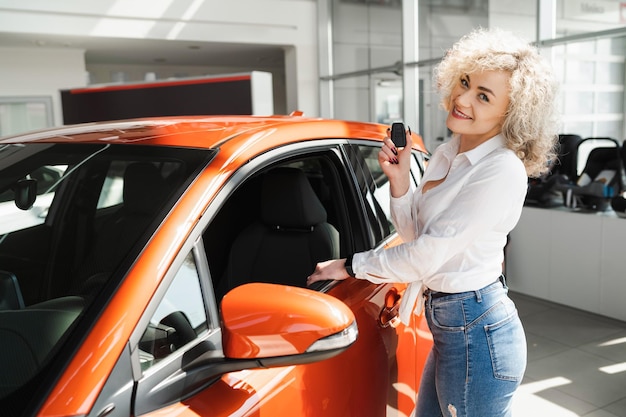 Happy woman with key near her new car in dealership