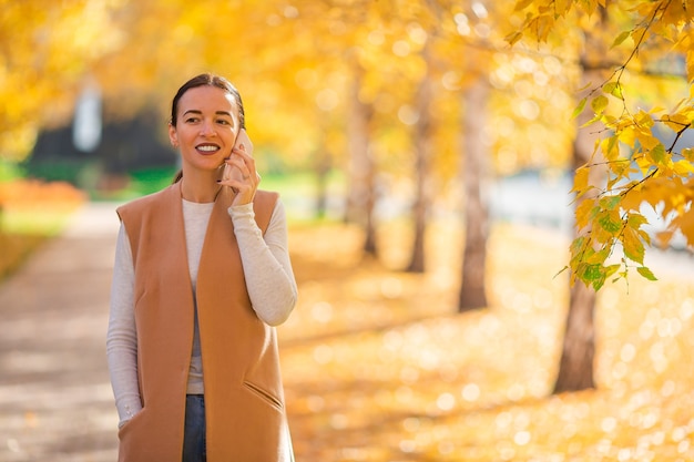 Happy woman with smarphone in autumn park under fall foliage. Golden autumn park