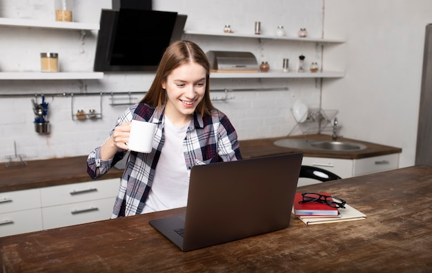 Happy woman working at home in the morning. Young girl yawns. She is using her laptop