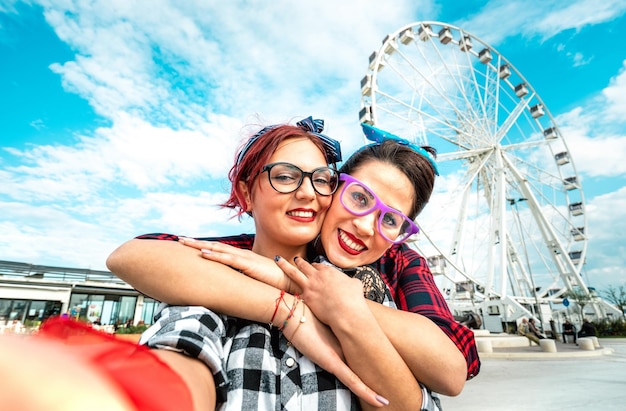 Happy women girlfriends taking selfie at ferris wheel on public area