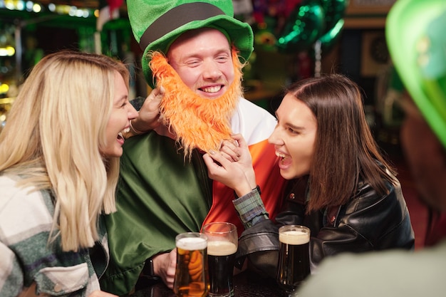 Happy women laughing about costume of young man while celebrating Patriks Day in the pub