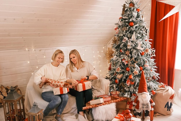 Happy women mothers are preparing for Christmas, New year pack gifts at home while sitting near Christmas tree. Winter holidays, home decoration concept