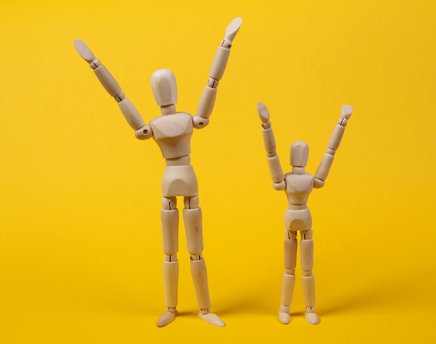 Happy wooden puppets with hands raised up on yellow background. Positive emotions