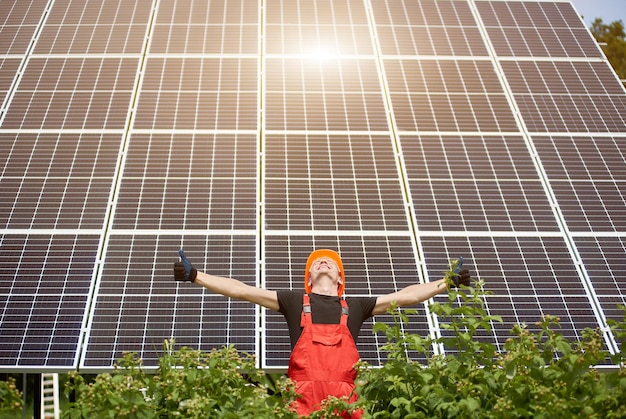 Happy working solar station raising his hands on a background of photovoltaic panels