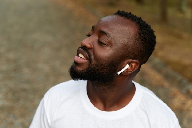 Happy young adult african american man walking in the park wearing headphones