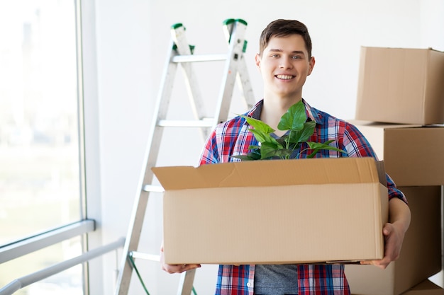 Happy Young Adult Man Holding Moving Boxes In Empty Room In A New House.