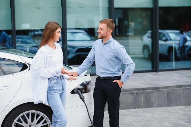 Happy young adult man and smiling woman charging electric car