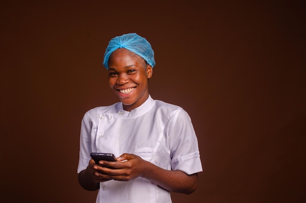 Happy young African doctor in scrubs texting with smartphone inside empty hospital