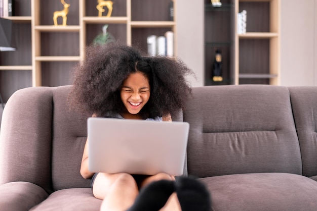 Happy young african girl using laptop and internet online at home