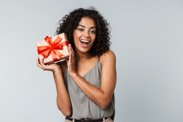 Happy young african woman casually dressed standing isolated, holding a gift box