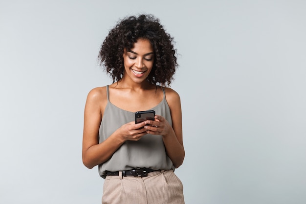 Happy young african woman casually dressed standing isolated, using mobile phone