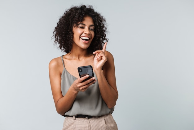 Happy young african woman casually dressed standing isolated, using mobile phone