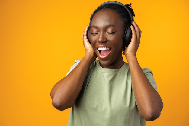 Happy young Afro American woman listening to music in headphones against yellow background