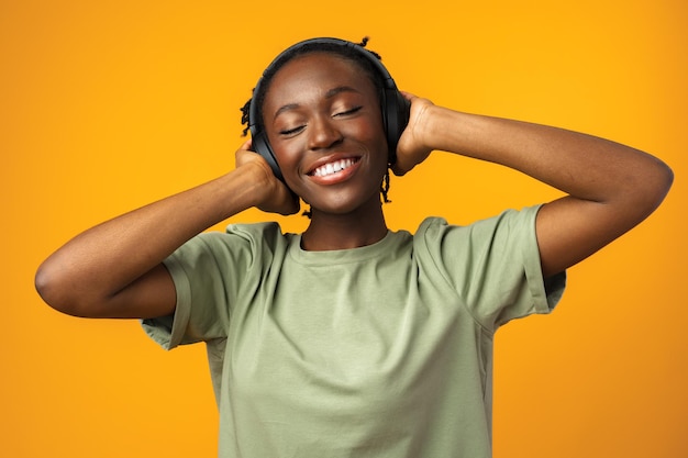 Happy young afro american woman listening to music in headphones against yellow background