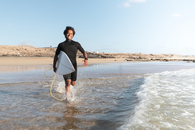 Happy young afro surfer running to the waves on the beach shore