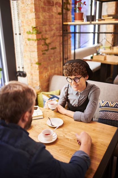 Happy young amorous couple sitting in cozy cafe or restaurant, having tea and discussing their plans