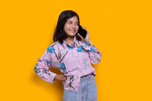 happy young asian beautiful woman using mobile phone isolated on yellow background