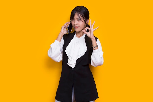 happy young asian beautiful woman using mobile phone isolated on yellow background