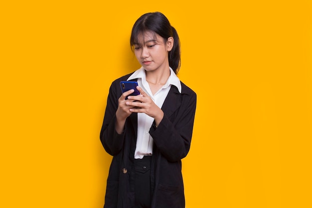 happy young asian business woman using mobile phone isolated on yellow background