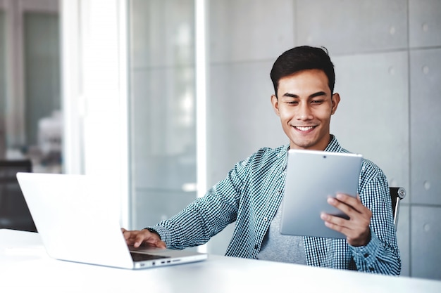 Happy Young Asian Businessman Working on Computer Laptop in his Workplace