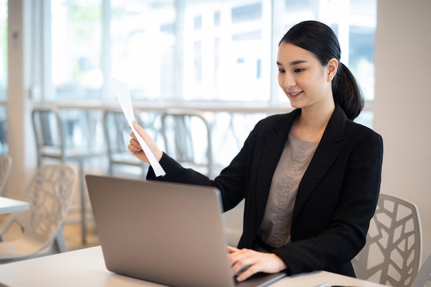 Happy young asian businesswoman sitting on her workplace in the office. Young woman working at lapto