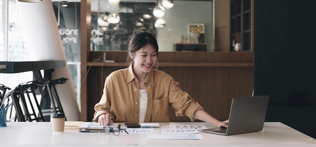 Happy young asian businesswoman sitting on her workplace in the office Young woman working at laptop in the officexA