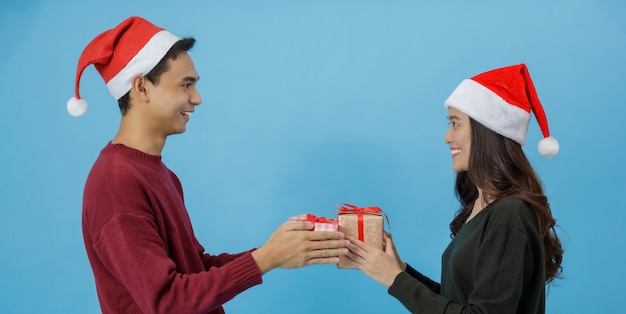 Happy young Asian couple holding Christmas gift boxes with happy smiling face isolated on blue background in studio shot.Christmas celebration of lover concept.