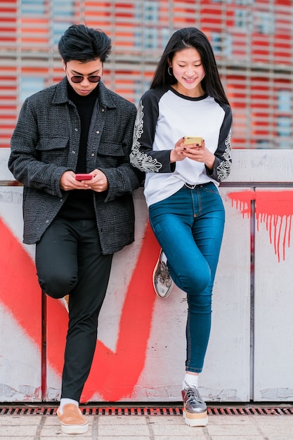 Happy young asian couple using smartphone on city street