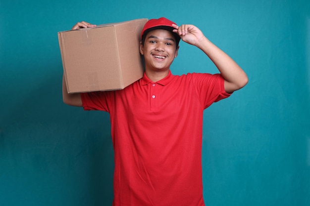 Happy young Asian delivery man in red uniform carry cardboard box on the shoulder