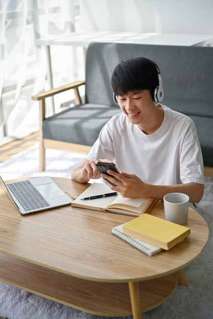 A happy young Asian man is listening to music at a coffee table in the living room