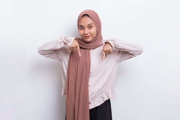 Happy young asian muslim woman pointing with fingers to different directions on white background