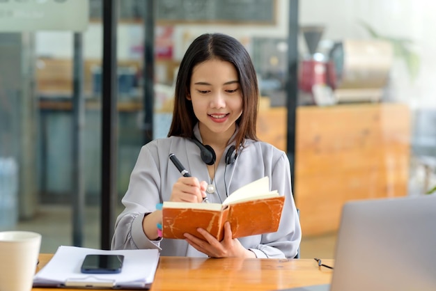 Happy young Asian student woman wearing headphones looking at webcam looking at camera during virtual meeting or video call talk